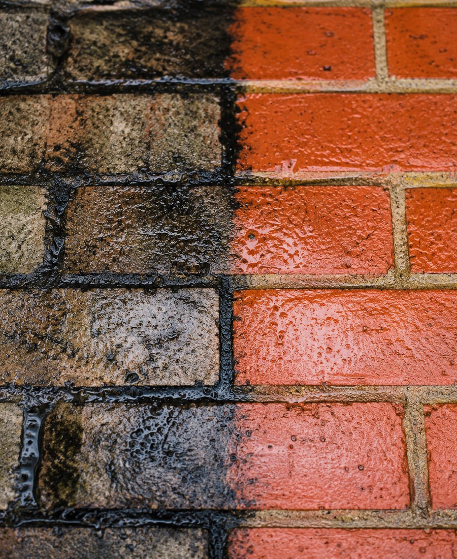 A brick wall shown half grimy and half cleaned back to bright red